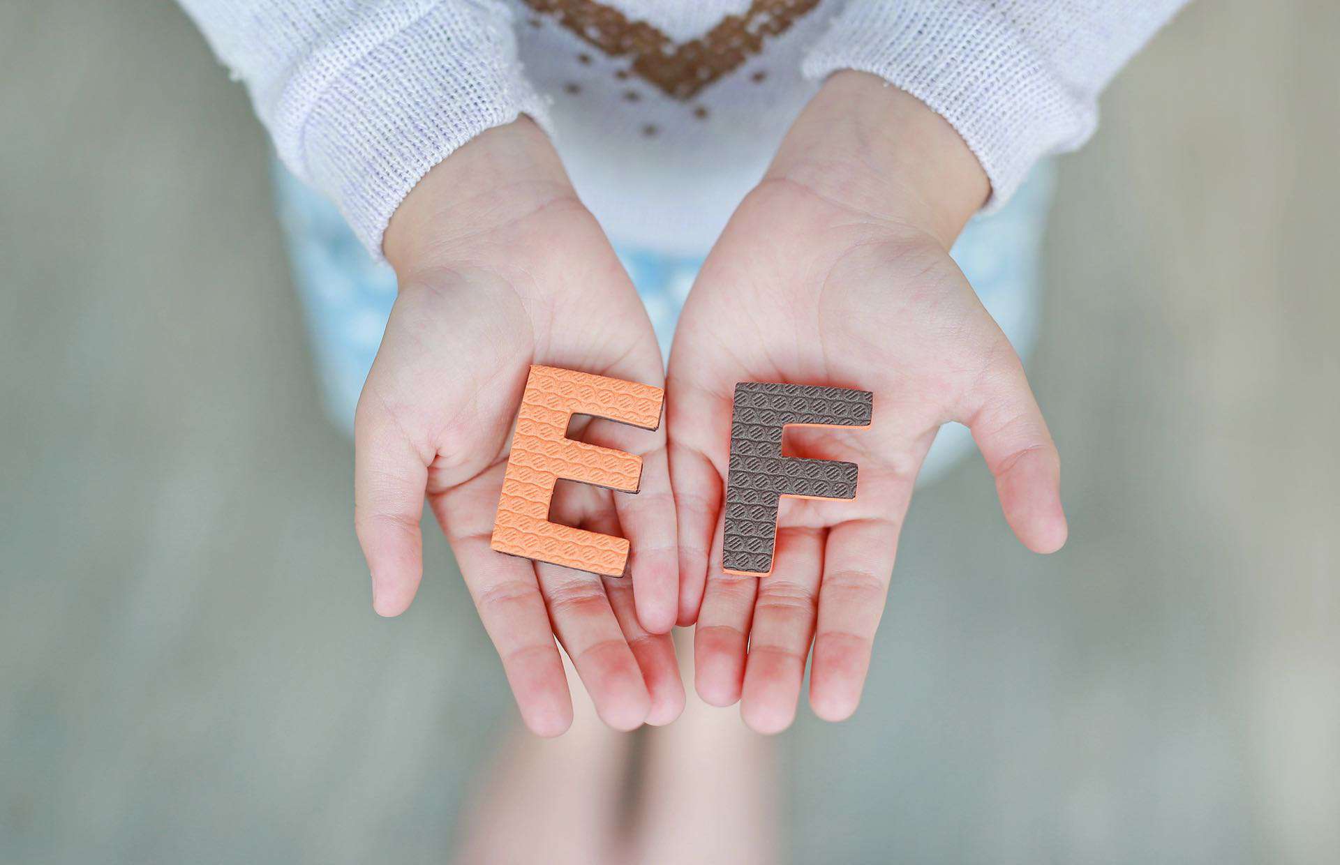 Een persoon met een lichte huid houdt twee getextureerde letters in zijn uitgestrekte handen. De oranje letter